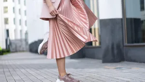 Pleated skirt coral color and sneakers. The girl is very dynamic posing on the street, the skirt is developing.