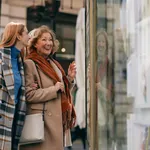 Happy grandmother and granddaughter looking at show window at the gallery.