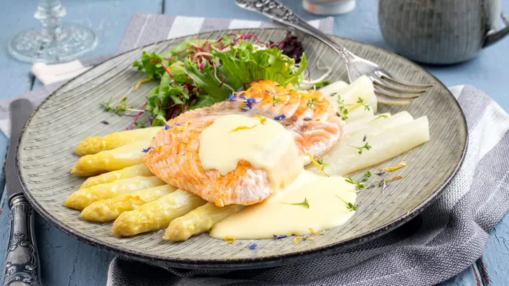Modern style Altantic fried salmon filet with traditional white asparagus in sauce hollandaise and lettuce service as close-up on a Nordic design plate