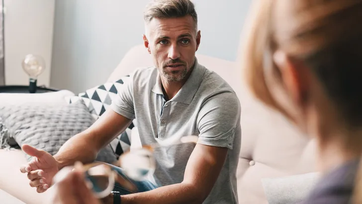 Photo of brooding handsome man having conversation with psychologist in room