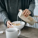 Cropped shot of young Asian mother preparing healthy breakfast, pouring milk over cereals on the kitchen counter. Healthy eating lifestyle