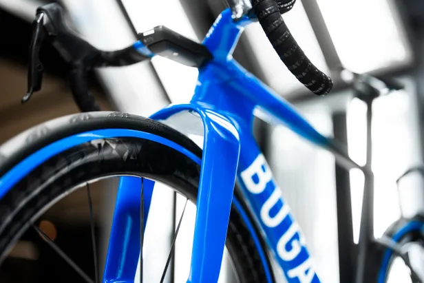 Close-up van de aerodynamische voorvork en het voorwiel van de Factor x Bugatti fiets, die de brede ruimte toont die de UCI-regels overschrijdt.