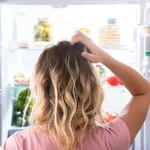 Confused Woman Looking In Open Refrigerator