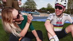 Tadej Pogacar zit in regenboogtrui op het gras en lacht met Urska Zigart na afloop van Parijs-Roubaix