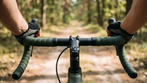 Ontspannen handen op een dik, comfortabel stuurlint van een gravelbike, met uitzicht op een zonnig bospad