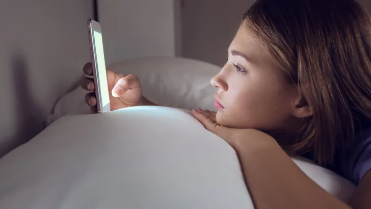 Teenage girl with mobile phone lying in bed at night