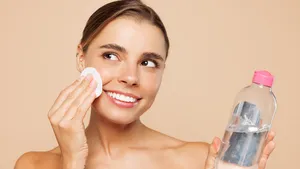 Jonge vrouw van in de twintig met make-up gebruikt micellair water om haar gezicht te reinigen