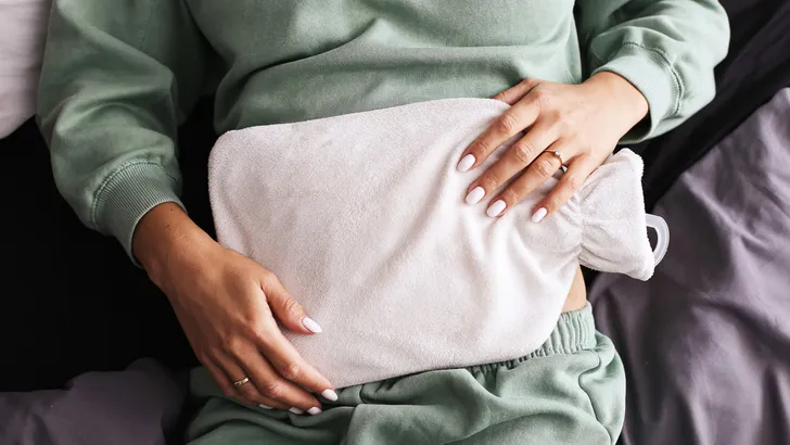 Warmwaterkruik op de buik, illustratie bij artikel over de houdbaarheidsdatum en veiligheid van warmwaterkruiken.