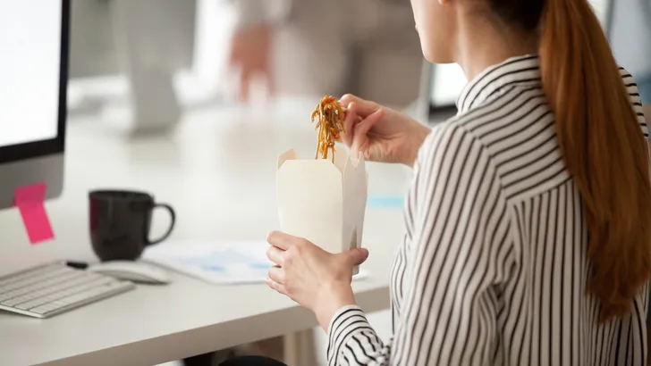 Female employee eating Asian noodles during office work break