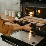 Young mother putting a tray full of cookies in the oven