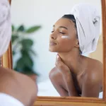 Perfect skin feels good. Cropped shot of an attractive young woman examining her face in the mirror at home.