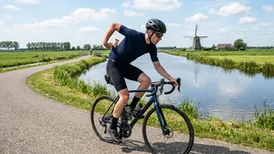 Mannelijke wielrenner op de racefiets in Nederlands landschap pakt voeding uit de achterzak van zijn fietsshirt.
