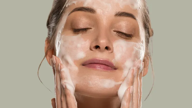 Close-up van een vrouw met schuimende cleanser op haar gezicht tijdens huidverzorgingsroutine