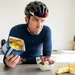 Wielrenner in fietskleding twijfelt in de keuken tussen een zak chips en een gezonde kom met kwark en fruit na zijn training