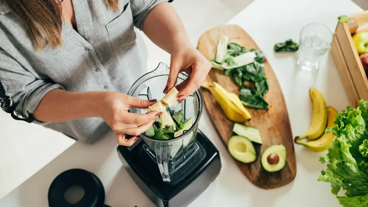 Woman is preparing a healthy detox drink in a blender - a  green smoothie with fresh fruits, green spinach and avocado