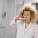 Vrouw staat voor de badkamerspiegel en poetst haar tanden met een flinke kater na oud en nieuw.