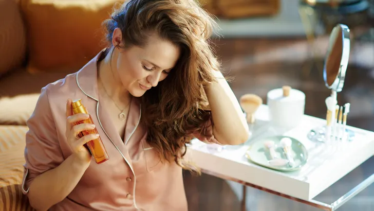woman holding hair oil at modern home in sunny winter day