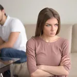 Angry sad woman standing with arms crossed, man in background