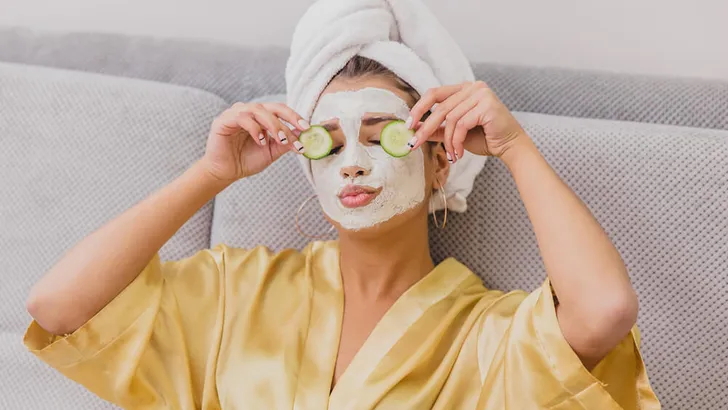 A beautiful young woman gets a face mask in the spa center, lying with cucumbers in her eyes. Happy and gets a lot of fun.