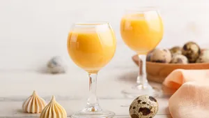 Sweet egg liqueur in glass with quail eggs and meringues on white wooden background. Side view, close up, high key.