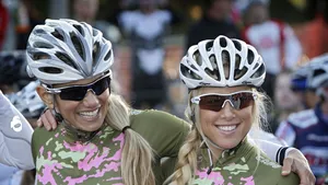 Twee lachende fietsers met helm en zonnebril staan arm in arm na een rit, vrolijke sfeer als uitnodiging om in 2026 te gaan fietsen.