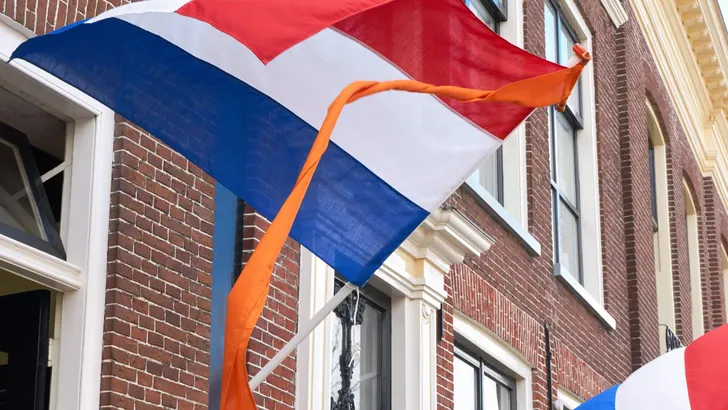 Dutch flags with orange streamer waving in the wind on facades of typical dutch houses on Koningsdag in the Netherlands. A national holiday in the Kingdom of the Netherlands