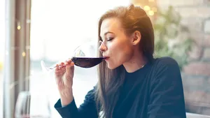 Beautiful young woman drinking red wine with friends in cafe, portrait with wine glass near window. Vocation holidays evening concept