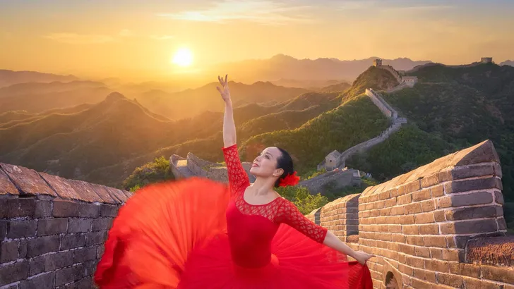 Chinese woman ballet dancer with red dress dancing at sunset in the Great Wall. Woman ballerina dance in ballerina shoes dancing with red silk gown flying on wind and the Great Wall at sunset. China