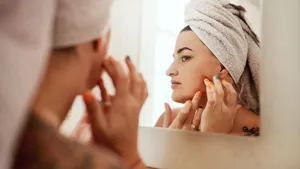 Vrouw die haar gezicht inspecteert als onderdeel van haar ochtendroutine voor huidverzorging in haar badkamer.