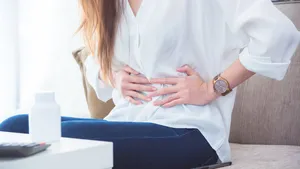 A woman having stomachache sitting on sofa and holding her belly by hands.