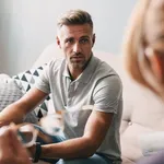 Photo of brooding handsome man having conversation with psychologist in room