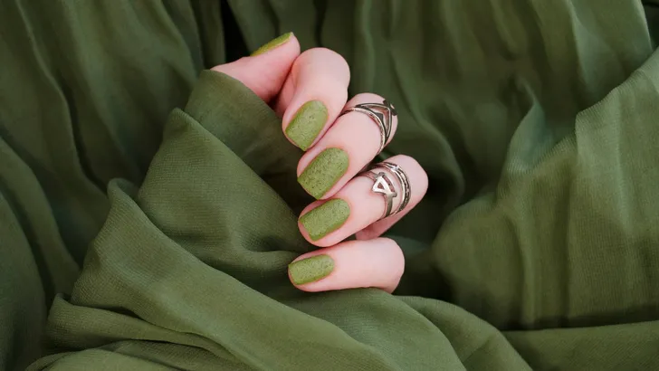 Closeup top view of beautiful painted in green nails isolated on green fabric background. Winter autumn nail style concept.