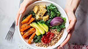 Woman hands eating vegan salad of baked vegetables, avocado, tofu and buckwheat buddha bowl, top view. Plant based food concept.