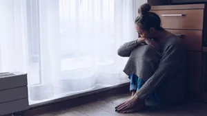 A devastated sad woman is sitting on the floor in her living room looking at the window.