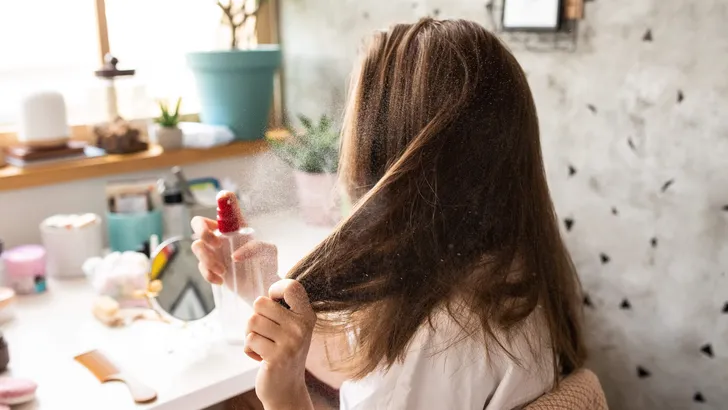 Young woman using hair spray in bedroom early in the morning