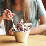 Female young lady eat Korean Bingsu ice with chocolate icecream. with ricecake and nuts. selective focus on bingsu blur people.