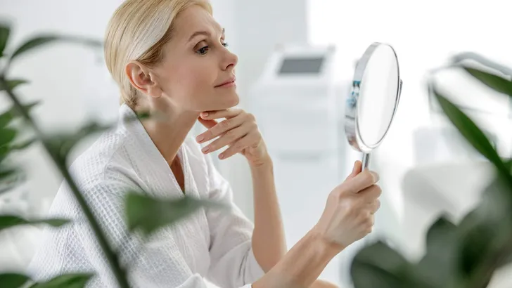 Smiling pretty woman using mirror in spa center