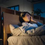 Young Asian woman feeling sick and suffering from a headache, lying on bed and taking a rest at home