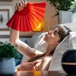 Heated beautiful woman fanning herself while sitting on couch at home.