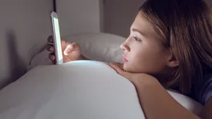 Teenage girl with mobile phone lying in bed at night