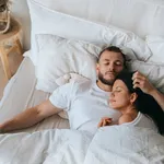 Young caucasian sleeping couple in bed. Handsome beardy European man laying with wife at bedroom enjoying Sunday morning. Calm hispanic young adult woman having nap at hotel with husband.