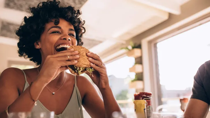 Woman enjoying eating burger at restaurant