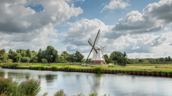 Polder landscape with canal and Witte Molen in Haren Glimmen in the Dutch province of Groningen to grind the water from the polder to the drainage system against background with cloudy sky