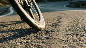 Close-up staande opname van een racefietsband die dynamisch contact maakt met een licht oneffen wegdek, waarbij de textuur van de band en het asfalt duidelijk zichtbaar zijn.