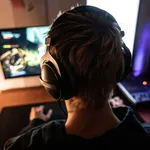 Rear View of Gamer with Headset on Playing Online Video Games in Dark Room - stock photo