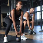 Fit and muscular couple focused on lifting a dumbbell during an exercise class in a gym.