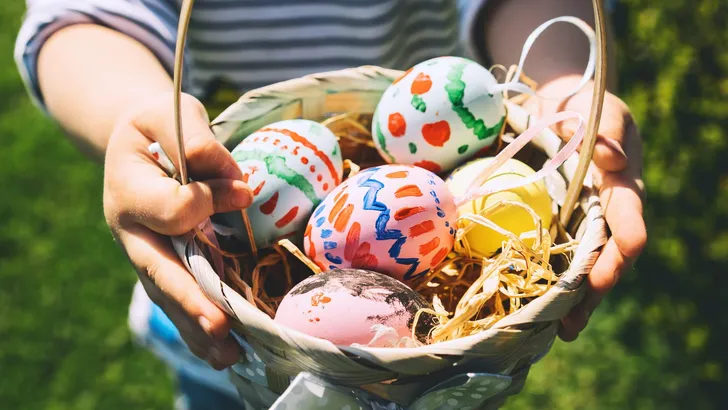 Colorful Easter eggs in basket. Children gathering painted decoration eggs in spring park. Kids hunt for egg outdoors.