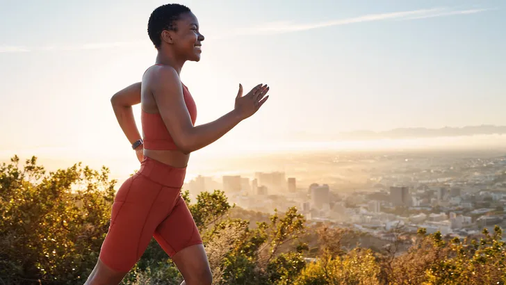Running, black woman and fitness on sunset mountains, city background and blue sky for exercise goals, energy and power. Happy athlete, cardio and outdoor workout with motivation, smile and wellness