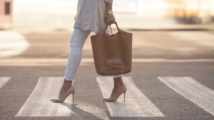 close up of woman legs walking on crosswalk. The woman is wearing shoes on high heels. Handbag in woman hand.