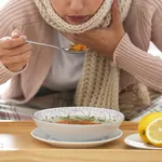 Sick young woman eating soup to cure flu at home, closeup